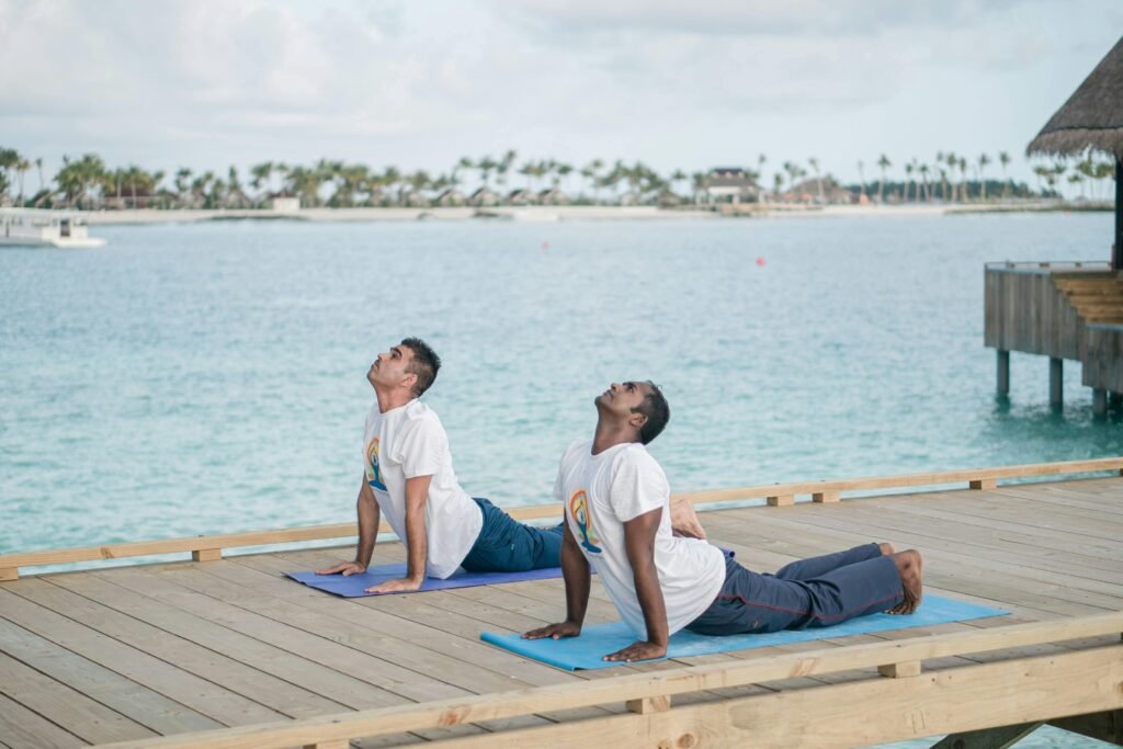 Two men practicing yoga on a deck overlooking the ocean on a sunny day.