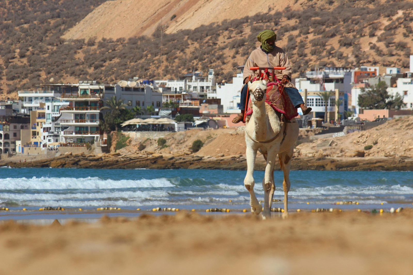 Gallery A man riding a camel along the picturesque beach of Taghazout, Morocco with scenic coastal views.