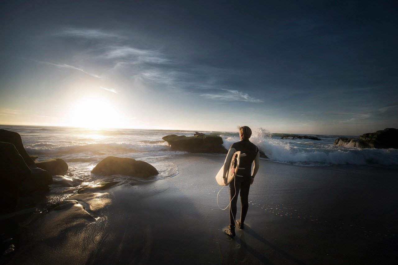 beach, ocean, surfer, surf, shore, seashore, waves, ocean waves, sunset, dusk, twilight, rocks, sand, sea, man, seascape, nature, sky, sun, sun glare, surfboard, water