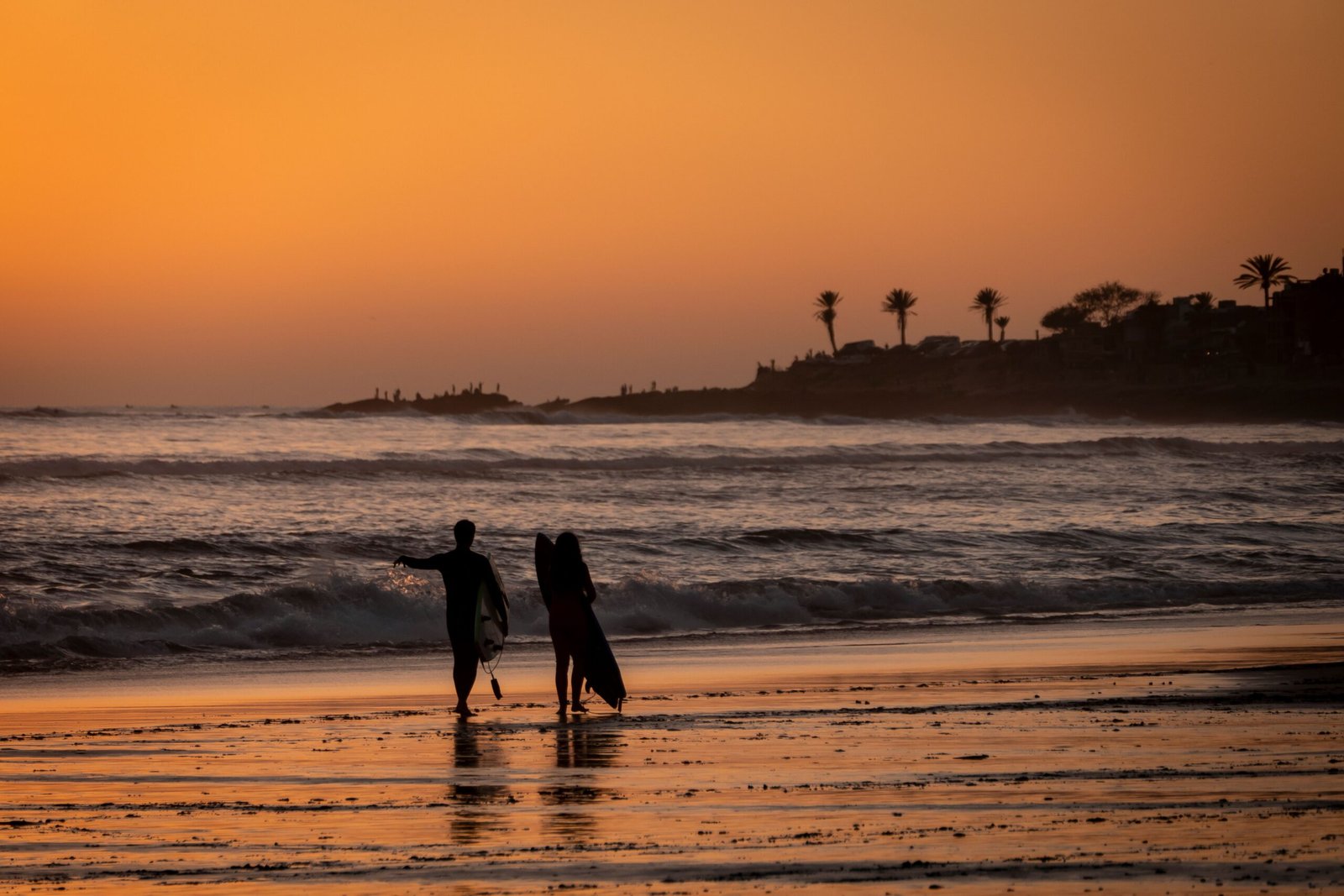 Gallery A beautiful sunset on the beach in Taghazout, Morocco, with surfers walking along the shore.