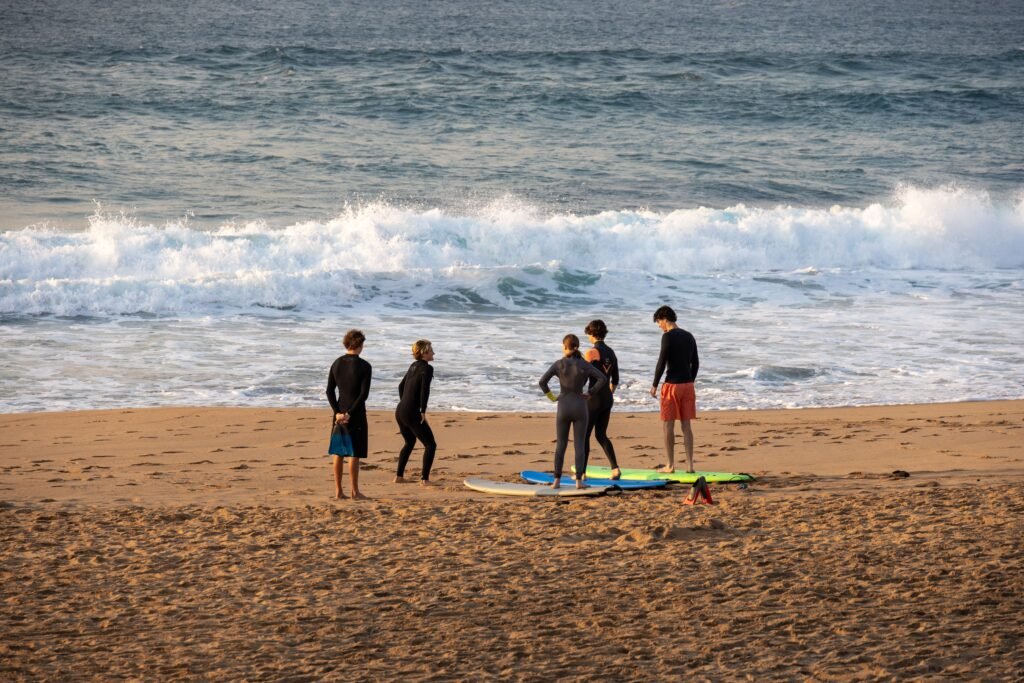 A group of adults preparing for a surf lesson on a sunny beach with waves crashing in the background.